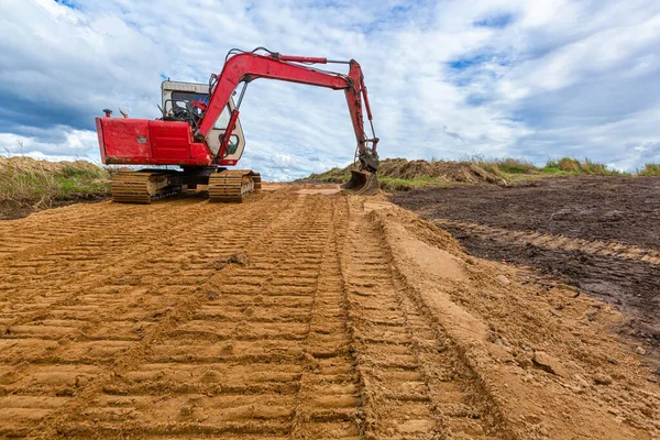 Nowoczesny koparka wykonuje prace wykopaliskowe na drodze piaskowej.Budowa dróg i pracy maszyn budowlanych. — Zdjęcie stockowe