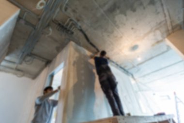 Bokeh 'teki işçiler. Erkekler dairenin tavanına elektrik kabloları döşüyorlar. İnşaat, tadilat, yenileme, uzatma, restorasyon ve yeniden yapılanma devam ediyor. Ev kavramı