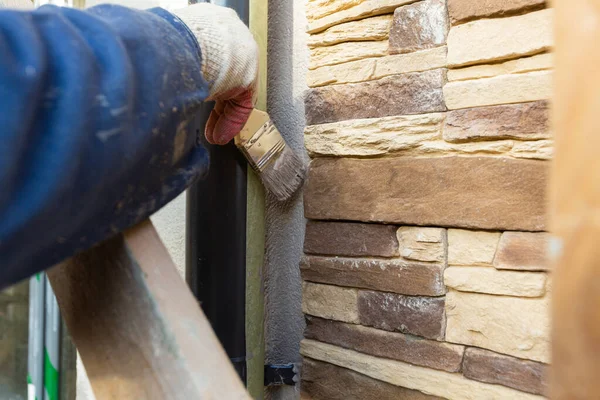 Operaio in guanti protettivi sta dipingendo con il pennello la casa di facciata che è in costruzione, ristrutturazione, ristrutturazione, estensione, restauro e ricostruzione. Concetto di miglioramento domestico o — Foto Stock