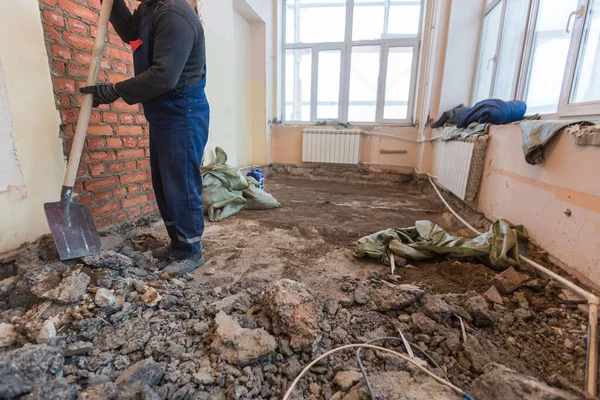 Werkproces van schoonmaken met schep na demontage en demontage van de vloer in de kamer van het appartement is dat in aanbouw, verbouwing, renovatie, uitbreiding, restauratie en wederopbouw Stockafbeelding