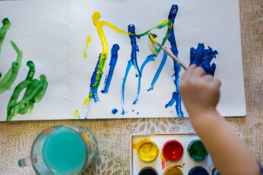 Küçük çocuğun üst görüntüsü kağıda parlak boyalar çiziyor.