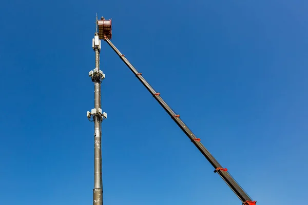 Ingeniero está trabajando en la torre de telecomunicaciones - teléfono celular repetidor mástil - de una plataforma de trabajo aéreo, también conocido como un dispositivo aéreo, plataforma de trabajo elevadora, selector de cerezas, camión cubo Imagen De Stock