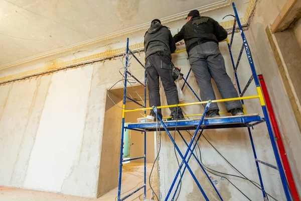 Двое рабочих монтируют электрические провода на стене, которая является частью внутренней отделки в строящейся квартире. — стоковое фото