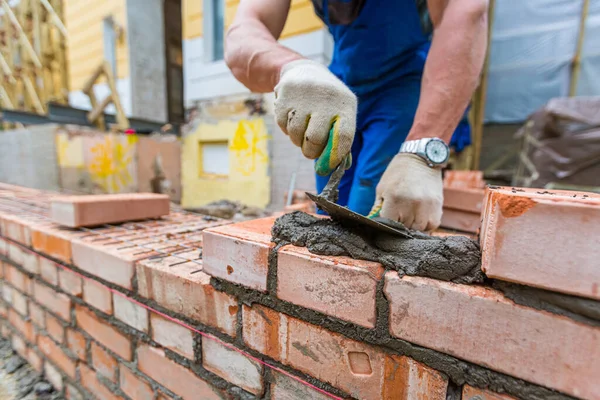 Bricklayer układa cegły na zewnętrznej ścianie z nożem szpachlowym na placu budowy. — Zdjęcie stockowe