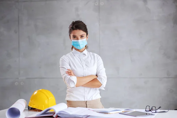 Young female architect with face mask standing with arms crossed during corona virus. Although it is corona outbreak architects have to work.