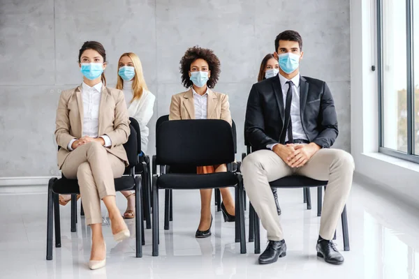 Multicultural group of business people with face masks sitting on seminar and listening during corona outbreak.