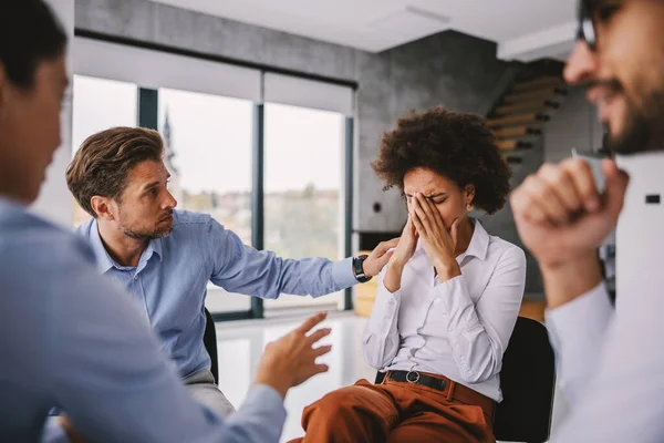 Desperate mixed race businesswoman crying because she lost her job. Her colleagues sitting around her and comforting her.