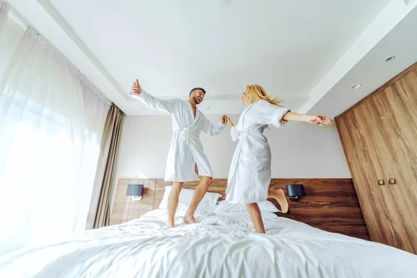 Cheerful Middle Aged Couple Bathrobes Celebrating Anniversary Hotel Weekend Jumping — Stockfoto