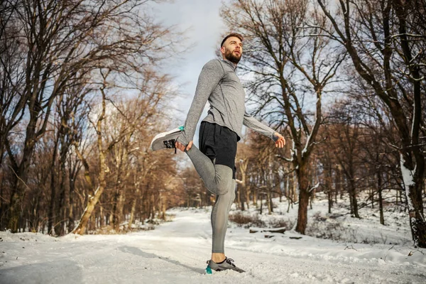 Runner doing warm up exercises in nature at snowy winter day. Winter sport, snowy weather, warm up exercises