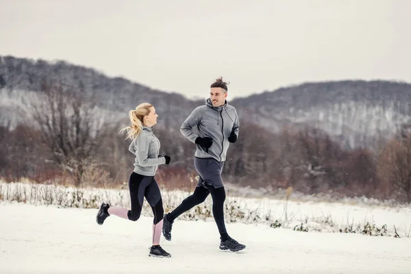 Happy fit sporty couple running in nature at snowy winter day. Outdoor fitness, healthy life, winter fitness