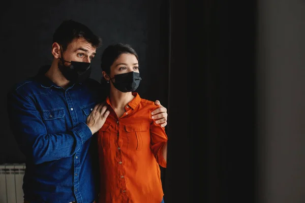 Casal Assustado Com Máscaras Faciais Lado Janela Olhando Para Fora — Fotografia de Stock