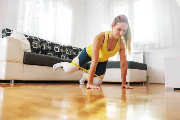 女运动员跪在家里的地板上 用腿伸展动力橡胶 大腿练习 — 图库照片