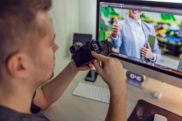 Creative work in advertising and marketing agencies. A man at work holds a camera in his hands while looking at a digital computer screen with a photo he has taken. Preparation for material editing