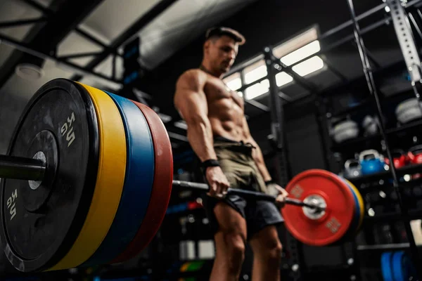 Weightlifting and the concept of sports life. A half-naked man stands in the middle of the gym and raises a barbell with weight plates. Dead lift with high load. Strength and energy, bodybuilding