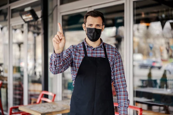 Catering facility and corona virus. A waiter in uniform and with a protective face mask stands in front of the entrance to the restaurant and forbids entry without virus protection. Restaurant work