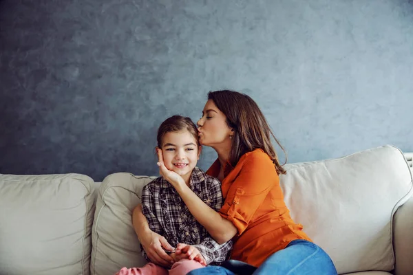 快乐的母亲坐在沙发上拥抱和亲吻她心爱的女儿 快乐的家庭观念 — 图库照片