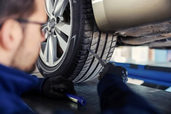 对汽车进行技术检查 检查轮胎 一个身穿蓝色制服的男人站在车间车库解决了一个汽车问题 一个戴眼镜的男人 一个在工作的男人的特写 — 图库照片