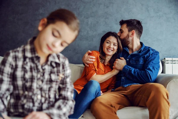 母親と父親がソファに座っている間に子供の絵を描く 抱擁とキス 親に焦点を当てます 幸せな家族 — ストック写真