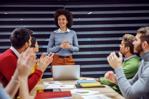 Presentation of a project idea. A multicultural group of businesspeople having a meeting at the town hall. The mixed businesswoman stands and explains the idea while her colleagues sit and clap