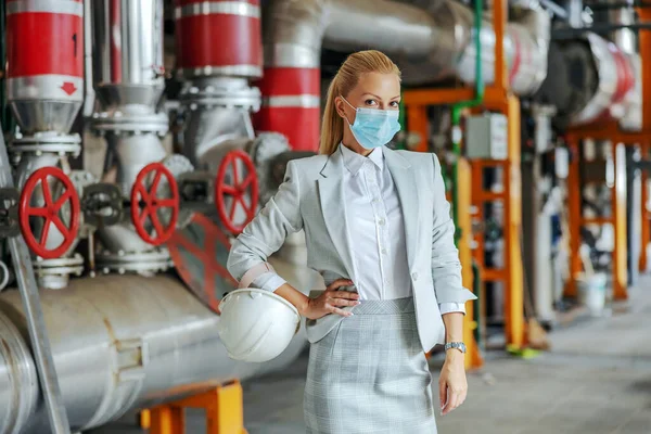 A portrait of a woman in an elegant suit in a work environment. Middle-aged successful businesswoman in formal wear standing in the heating plant during corona virus pandemic