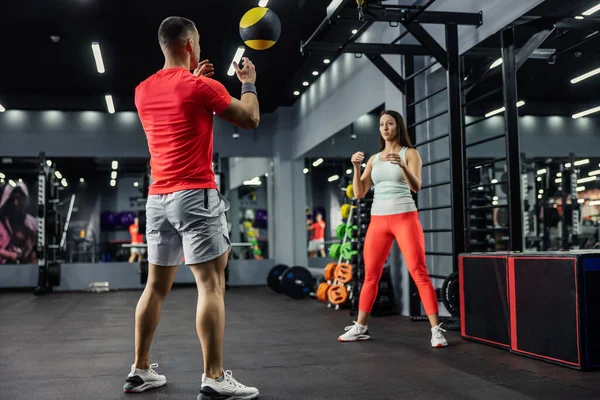 スポーツウェアの女性と男性はお互いを見て ジムでフィットネス医学ボールを投げ 焦点と体全体のための演習を行います フィットネスの課題 いくつかの目標 — ストック写真