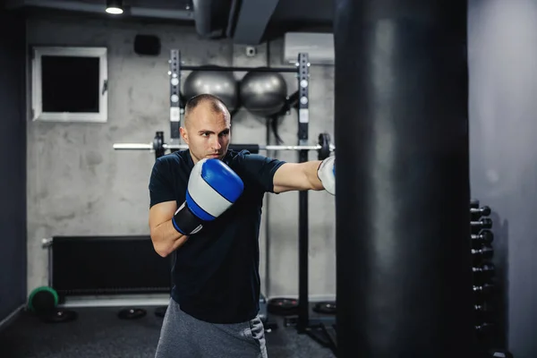 Boxing training. Male boxer hitting a black punching bag at a fitness studio. Male adult boxer wearing gloves and training hard indoor gym. Fitness goal, motivation on training, kicking bag