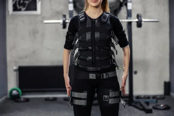 Electrical muscle stimulation. A body part portrait of a satisfied beautiful woman in a special EMS suit standing in the middle of the gym. Good physical form of the modern concept of training no face