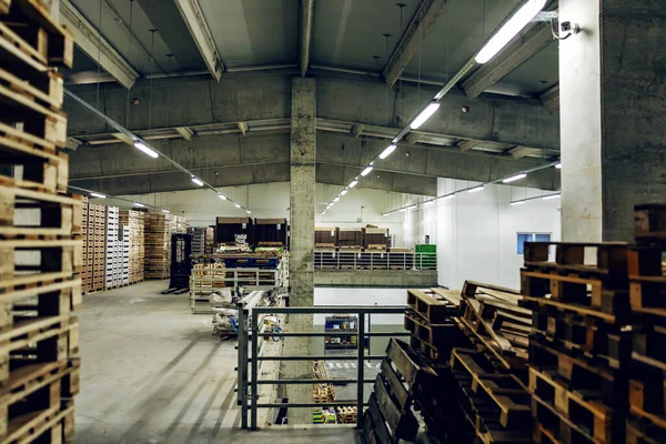 Warehouse with a pile of wooden pallets. Large empty hall without people on two floors with concrete walls and pillars and with many pallets. Stocks of raw materials for distribution and logistics