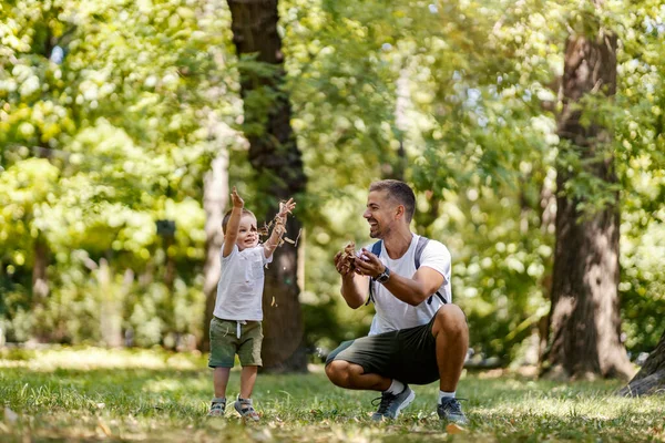 Happy childhood and growing up. A father and son dressed in the same clothes play in the woods one summer day. They throw leaves up and laugh at each other. Escape to nature for family weekend