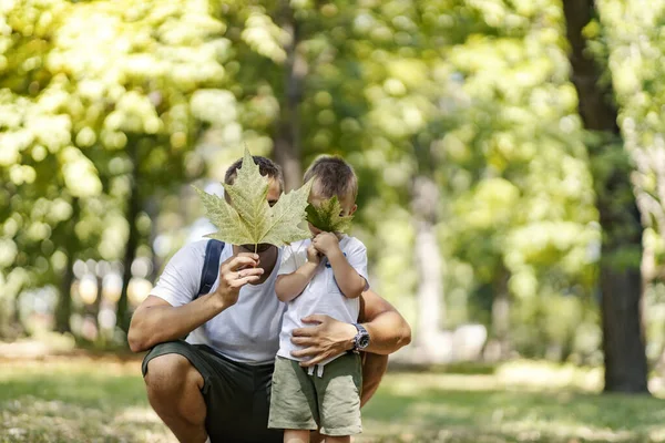 Escape to nature and an active weekend. Holidays in the woods, family fun in the park. Father and son are dressed in the same clothes fooling around with leaves Dad squats next to the boy and hugs him