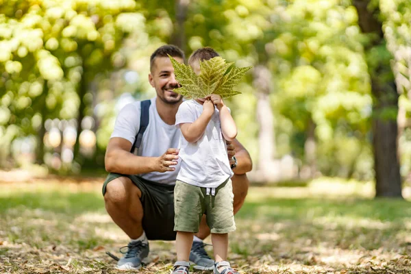 Vacation in the woods, family fun in the park, escape to nature and active weekend. A father and son are dressed in the same clothes. Boy holds a leaf in front of his face while dad posing for a photo
