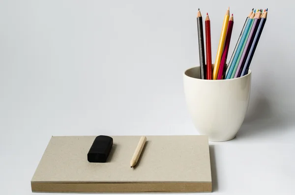 Notebook com lápis e lápis de cor no vidro sobre fundo branco — Fotografia de Stock