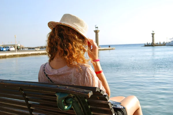 Mädchen sitzt auf Bank am Pier. lockiges Haar. Hut — Stockfoto