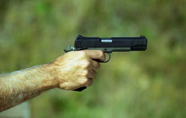 Closeup of man holding semi automatic firearm with hammer back preparing to shoot.