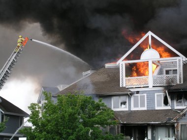 İtfaiyeciler yanan bir eve itfaiye arabasının kulesinden su döküyorlar..