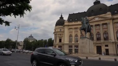 Bükreş, Romanya - 22 Ekim 2020 - Bükreş Ulusal Merkez Üniversitesi Kütüphane Binası ve Romanya Kralı I. Carol 'un Heykeli' nin 4k videosu. Yoldan geçen arabalarla seyahat videosu. Şehirde trafik vardı.