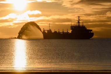 Gün batımında tarama yapan bir gemi. Hopper dredger denizde çalışıyor. Su ortamında kazı yapan bir gemi. Güzel gün batımı.