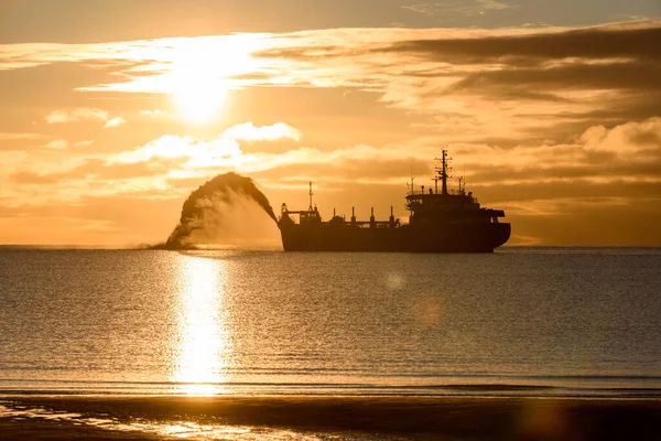Gün batımında tarama yapan bir gemi. Hopper dredger denizde çalışıyor. Su ortamında kazı yapan bir gemi. Güzel gün batımı.