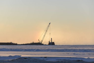 Vinçli mavna. Dredger denizde çalışıyor. Kutup Denizi 'nde gün batımı. Deniz aşırı inşaat işleri. Baraj inşaatı, vinç, mavna, eşeleme.