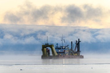 Gemi tarama yapıyor. Dredger denizde çalışıyor. Su ortamında kazı yapan bir gemi. Kuzey Kutup Denizi 'nde yoğun sis var. Deniz aşırı inşaat işleri. Baraj inşaatı, vinç, mavna, eşeleme.