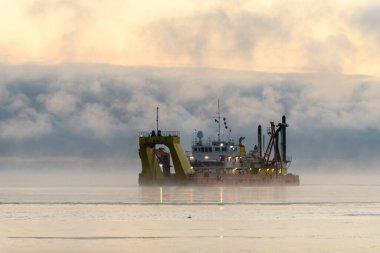 Gemi tarama yapıyor. Dredger denizde çalışıyor. Su ortamında kazı yapan bir gemi. Kuzey Kutup Denizi 'nde yoğun sis var. Deniz aşırı inşaat işleri. Baraj inşaatı, vinç, mavna, eşeleme.