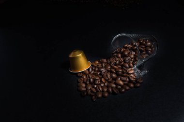 Kahve çekirdeği ve kahve fincanı ile ev yapımı kahve kapsülü makinelerinin soyut ve kavramsal hali. Siyah arka planda izole edilmiş espresso kahve kapsülleri koleksiyonu, yakın plan görüntü detayları. Kopyalama alanı olan grafiksel kaynaklar.