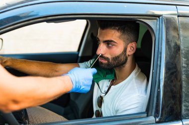 Coronavirüs enfeksiyonu için arabadaki bir adamdan burun temizleme örneği almak bir sağlık çalışanı Covid-19 için bir kontrol çubuğunu arabasında oturan bir adama verir.