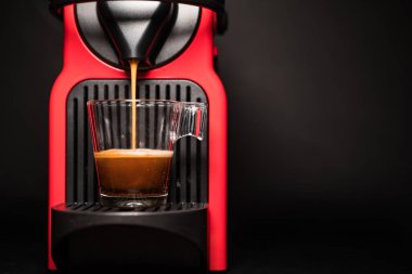 Kahve makinesiyle kahve makinesini cam şeffaf fincana çevirme işlemi - otomatikleştirilmiş kahve makinesinden çıkan espresso kahvesi - stüdyoda çok az izole edilmiş - siyah arka planda.
