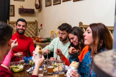 Kafkas gençleri barda yemek yiyor. Bir grup mutlu arkadaş restoran arkadaşlığı konseptinde kahvaltı yapıyorlar. Yeni normal yaşam tarzı konsepti, açık maskeli genç arkadaşlarla birlikte yemek yemek.