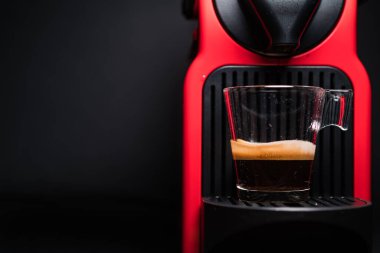 Kahve makinesiyle kahve makinesini cam şeffaf fincana çevirme işlemi - otomatikleştirilmiş kahve makinesinden çıkan espresso kahvesi - stüdyoda çok az izole edilmiş - siyah arka planda.