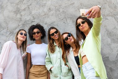Güneş gözlüklü mutlu bir grup kadın, güneşli bir günde akıllı telefonla selfie çekiyorlar. Arkadaşlık kavramı.
