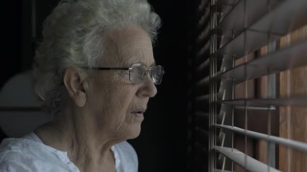 Old lady looks through window blinds — Stock Video