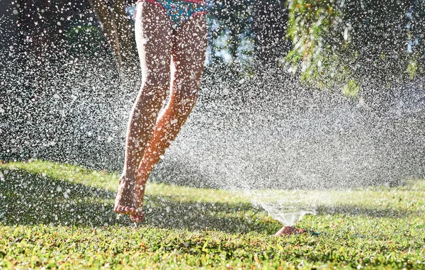 Lány játszik közelében víz sprinkler — Stock Fotó