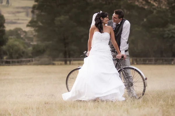 Νύφη και γαμπρός σε πεδίο με ποδήλατο — Φωτογραφία Αρχείου